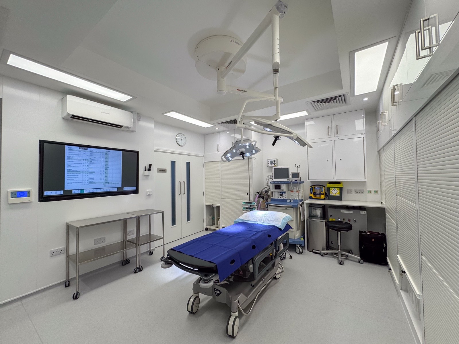 Second operating theatre at Kensington Cosmetic Clinic with surgical lighting and wall-mounted display